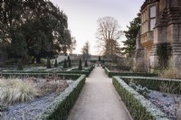 A path through the East Garden at The Bishop's Palace Garden in Wells on a January morning, framed by evergreen hedges of Euonymus japonicus 'Green Spire'.