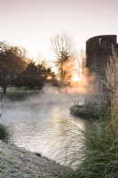 Morning sun illuminates mist rising from the moat at The Bishop's Palace in Wells in January.