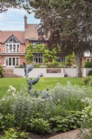 View across lawn to house with water feature and terrace from pastel border with wild duck sculpture