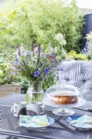 Table in garden with bouquet of flowers, hot drinks and freshly a baked cake
