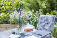Garden table with bouquet of flowers, hot drinks, plates and a freshly baked cake
