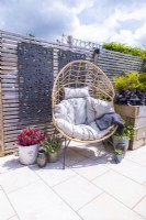 Wicker egg chair on white tile patio with decorative panels on fence and potted Fuchsia, Thyme, Alchemilla and sempervivum on the ground