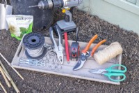 Wire, eyelet screws, ferrules, tensioners, pliers, pencil, tape measure, secateurs, string and scissors on wooden tray