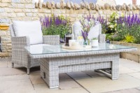 Wicker garden table and chairs on patio in front of raised bed
