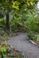 A log-edged gravel path through woodland planting leading to a bug hotel at The Picton Garden, Herefordshire