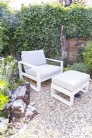 Seat and footstool in garden corner between borders with driftwood and rusted chain