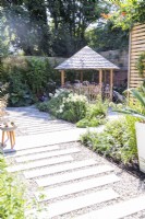 Garden with staggered stone tile path leading towards mixed bed planted with Verbena bonariensis, Alchemilla mollis, Hydrangea paniculum 'Bobo' and pittosporum with a round wooden gazebo behind