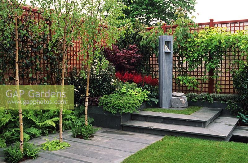 Red trellis fencing in corner of garden with slate sculpture and paving
