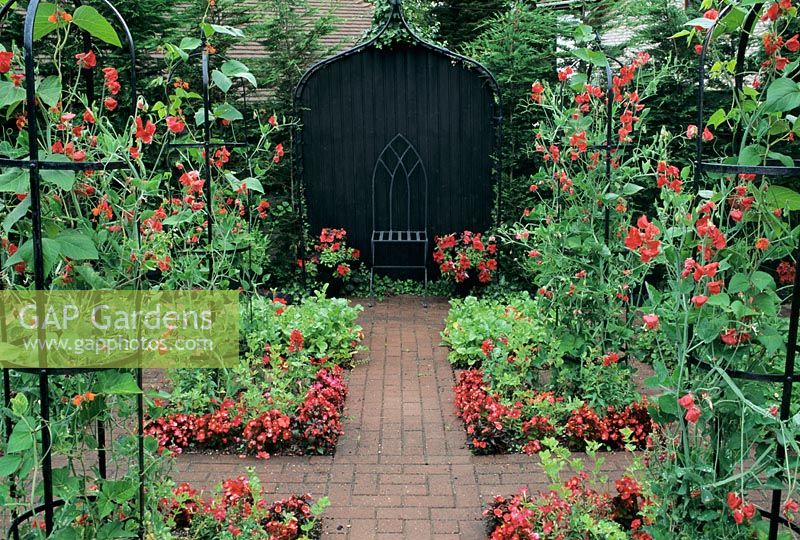 Covered seat in formal garden with Lathyrus - Sweetpeas Bouquet series (Scarlet) on obelisks in colour themed red garden at Little Cottage, Hampshire