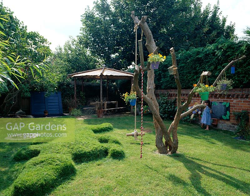 Childrens garden with dead tree, turf crocodile, trampoline, sandpit, blackboard, dipping pond and rustic wooden pole pergola