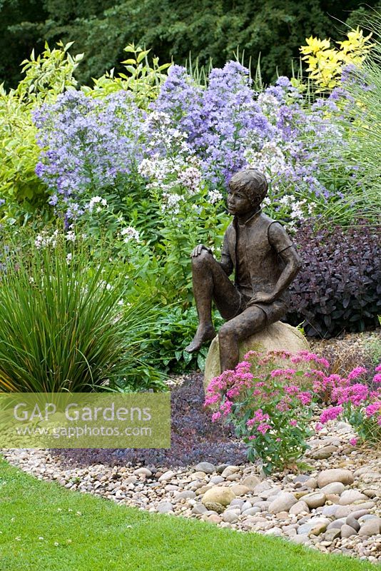 Summer border with statue 'Boy on the Rock' by Jane Hogben set on a boulder in a gravel bed