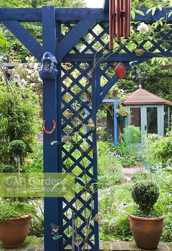 Overview of small densely planted courtyard garden looking through blue trellis to green painted summerhouse.
