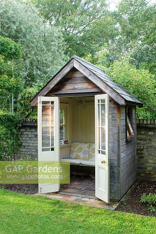 Small timber summer house with bench seat, french doors, painted wood panelling and slate roof. Made by the owner from an old garden shed and architectural salvage materials.