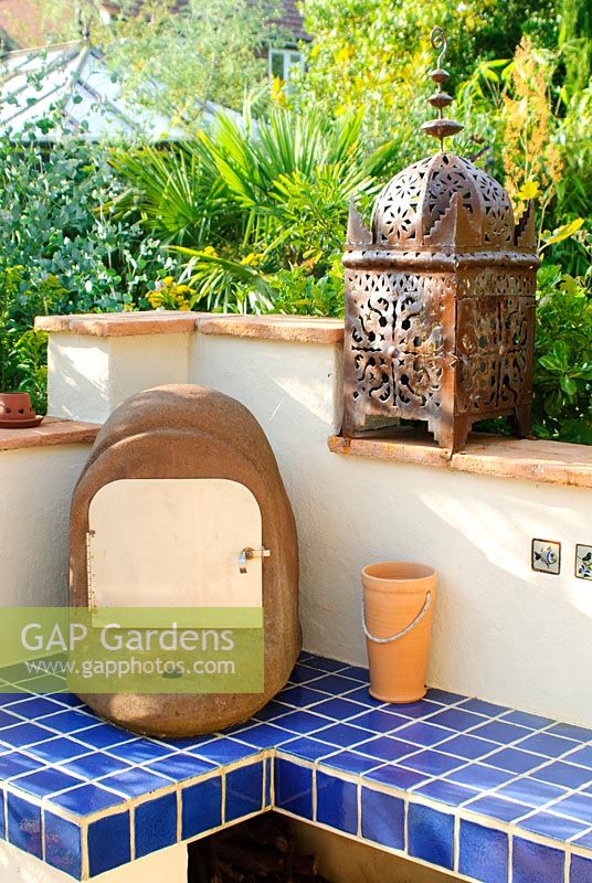 Outdoor oven on blue tiled plinth with Moroccan candle lantern on wall