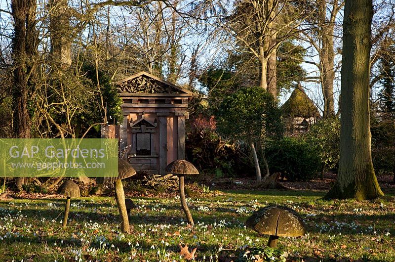 Wooden toadstool sculptures and one of the green oak temples, with  snow drops in the Stumpery, February 2011