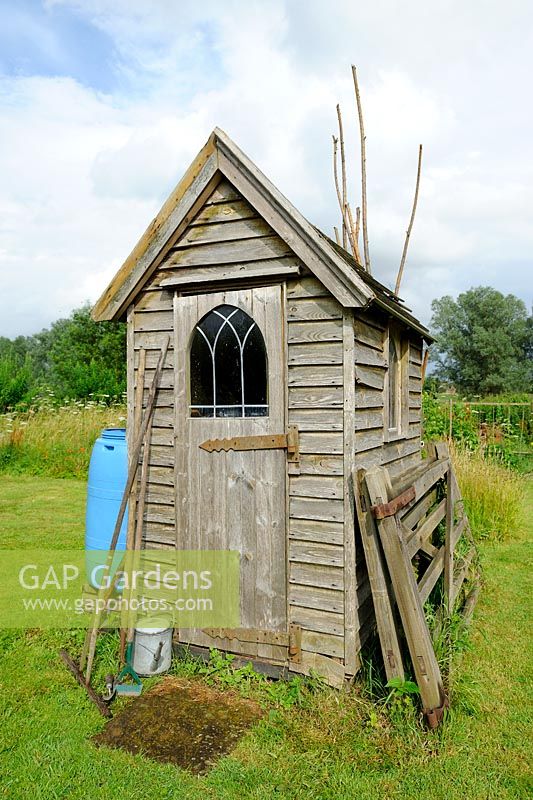 Small wooden garden shed with tools outside and blue water butt
