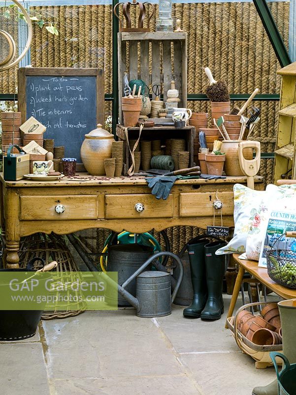 In greenhouse, old pine dresser provides work area for terracotta pots, string, labels, gloves and lists. Boots, watering cans, fork and trug.