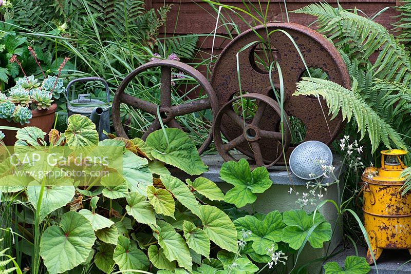 A decorative collection of metal industrial parts amongst begonia foliage and ferns.