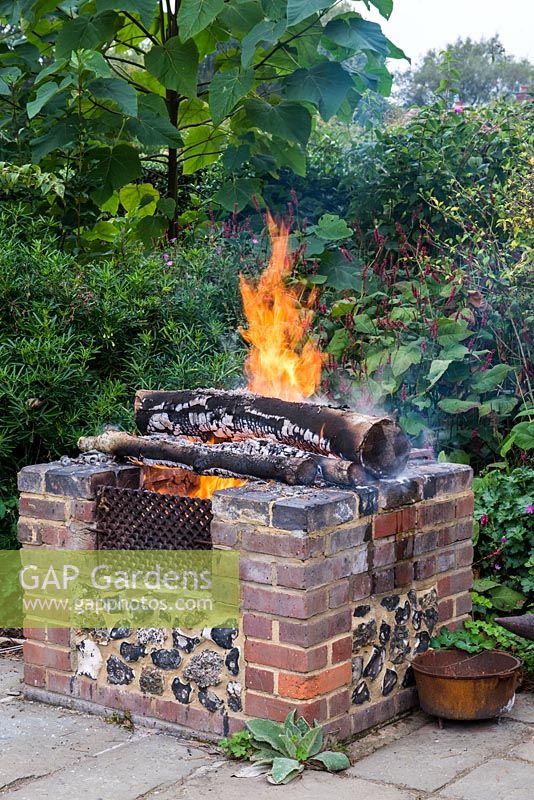 A raised brick fire pit warming the garden in late summer.