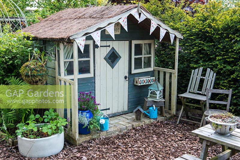 A children's wendy house with containers planted with herbs and strawberries.