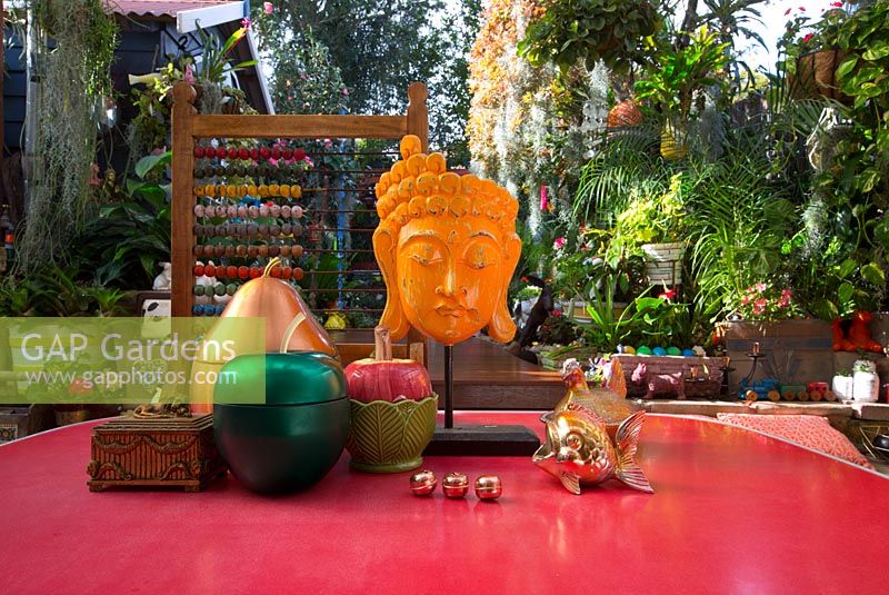 Eclectic ornaments on a red retro laminex table in covered outdoor entertaining area with Thai style mask, June.