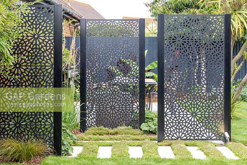 Black decorative screen dividing garden and providing privacy for seating area.