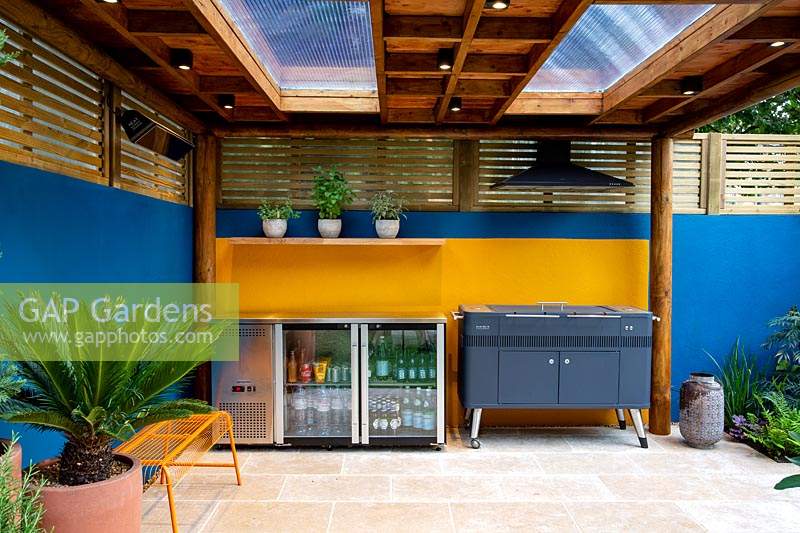 Outdoor room with barbecue and fridge. Surrounded by a contemporary wooden trellis fence and blue painted wall.
