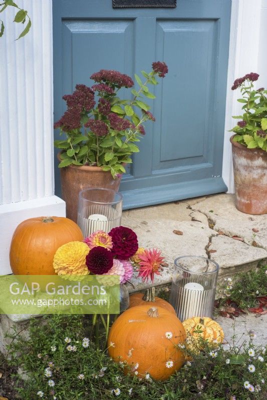 Front door and stone steps decorated for Halloween with pots of Sedums, squashes, flowers and candles 