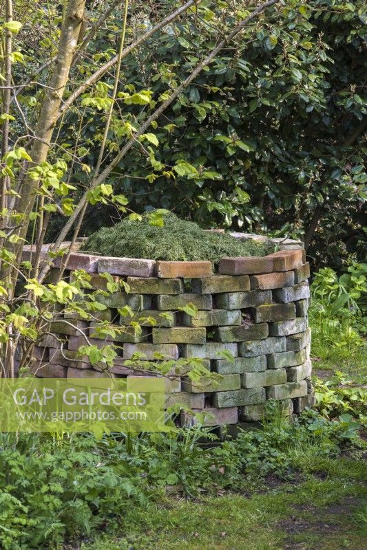 Temporary circular brick compost heap with grass cuttings