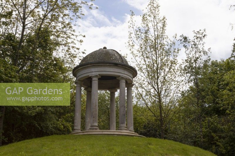 A domed classical temple on a grassy knoll. Trago Mills show gardens, Devon, UK. May. Spring