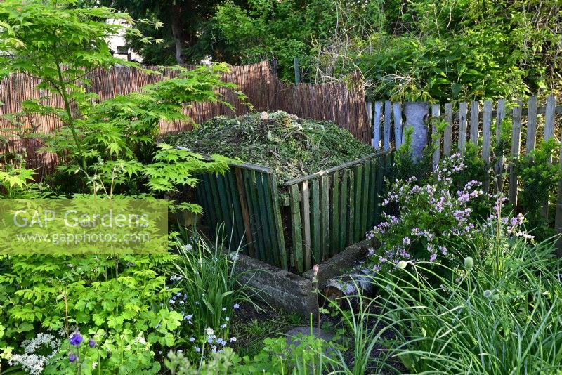 Wooden composter in the corner of the garden filled with fresh plants.