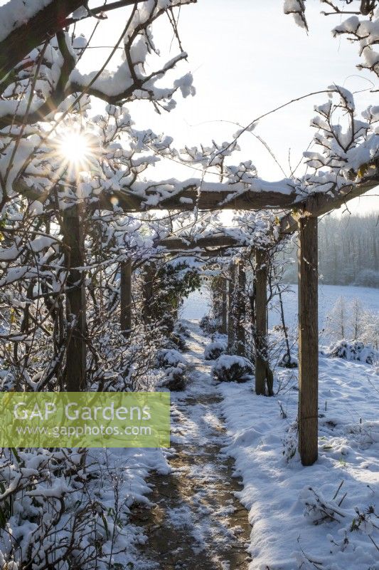 The garden at Gravetye Manor, Sussex, in winter. A view through a snow covered pergola