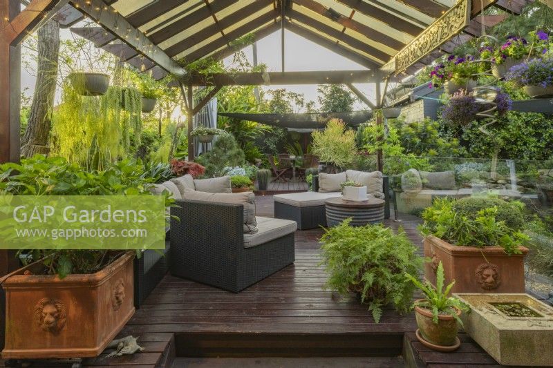 Outdoor patio and timber pergola with furniture, hanging baskets and potted plants.