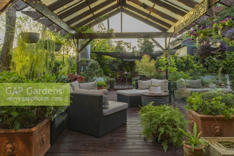 Outdoor patio and timber pergola with furniture, hanging baskets and potted plants.