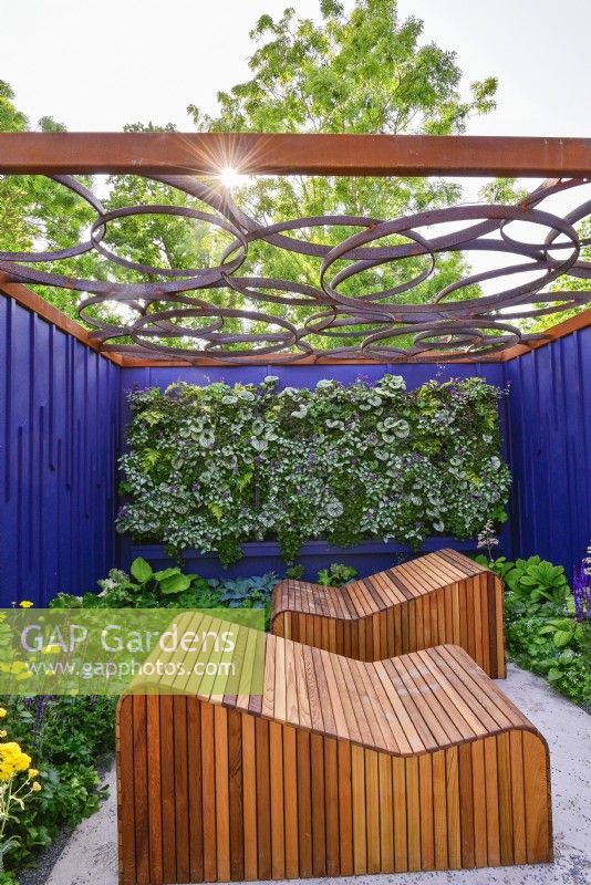 Relaxation area surrounded by a navy blue painted panels with decorative wooden deckchairs set against living green wall under with geometric design openwork of pergola roof.  June
Bord Bia Bloom, Dublin
Designer: Jane McCorkell



