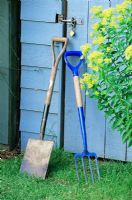 Spade and fork leaning up against blue wooden shed