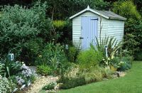 Gravel path leading to painted shed in seaside themed garden with Eryngiums, yuccas and phormium. Decorative use of painted spades