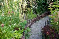 Gravel path edged with woven willow hurdles through herbaceous borders