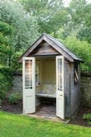 Small timber summer house with bench seat, french doors, painted wood panelling and slate roof. Made by the owner from an old garden shed and architectural salvage materials.