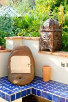 Outdoor oven on blue tiled plinth with Moroccan candle lantern on wall