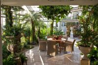 View into the glasshouse with tropical climate, wicker chairs and wooden table with a fruit arrangement. Planting includes Anthurium andreanum, Araucaria heterophylla, Beaucarnea recurvata, Billbergia nutans, Citrus sinensis, Cycas revoluta and Phoenix roebelinii - Wintergarten, Germany
