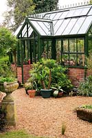 Green powder coated aluminium greenhouse built on a brick base in a Victorian style with ridge cresting and porch, filled with exotic plants and succulents