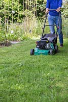 Woman mowing grass on an allotment patch