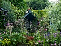 A secluded covered seat surrounded by cottage garden style planting, including Pimpinella major Rosea, Rosa mundi, Clematis, Digitalis, Papaver and Helleborus foetidus. 