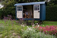 The Shepherd's Hut, a mobile summer house, behind a border of Verbena bonariensis, Anemone x hybrida and Sedum Autumn Joy. 
