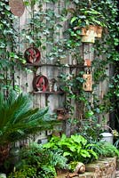 Ornate items on shelves. Planting of: Hedera helix, Hosta 'Sum and Substance', Pseudopanax crassifolius, Equisetum, Cycas revoluta, Crytomium falcatum and wooden wall. Lucille Lewins small court yard garden in Chiltern street studios, London. Designed by Adam Woolcott and Jonathan Smith 
