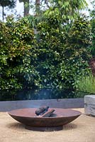 A rusty metal bowl fire pit on a paved area