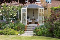 On one side of the summerhouse is a raised patio veiled by roses trained along a rope swag, the other Stipa gigantea 