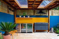 Outdoor room with barbecue and fridge. Surrounded by a contemporary wooden trellis fence and blue painted wall.