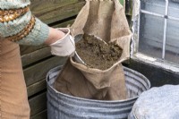 Creating a liquid feed for the garden using rotting vegetation in a hessian sack inside a bin.